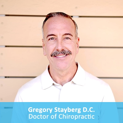 Chiropractor Gregory Stayberg In Front Of Wooden Wall With Caption